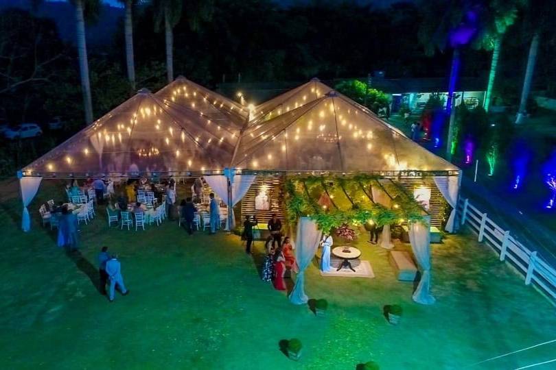 Chácara Soledade à noite: tenda transparente iluminada por luzes penduradas, cercada de palmeiras