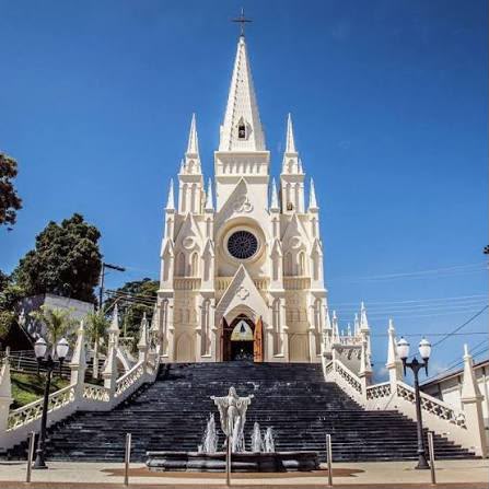 Fachada da Paróquia: igreja branca em estilo neogótico, com torres e escadaria